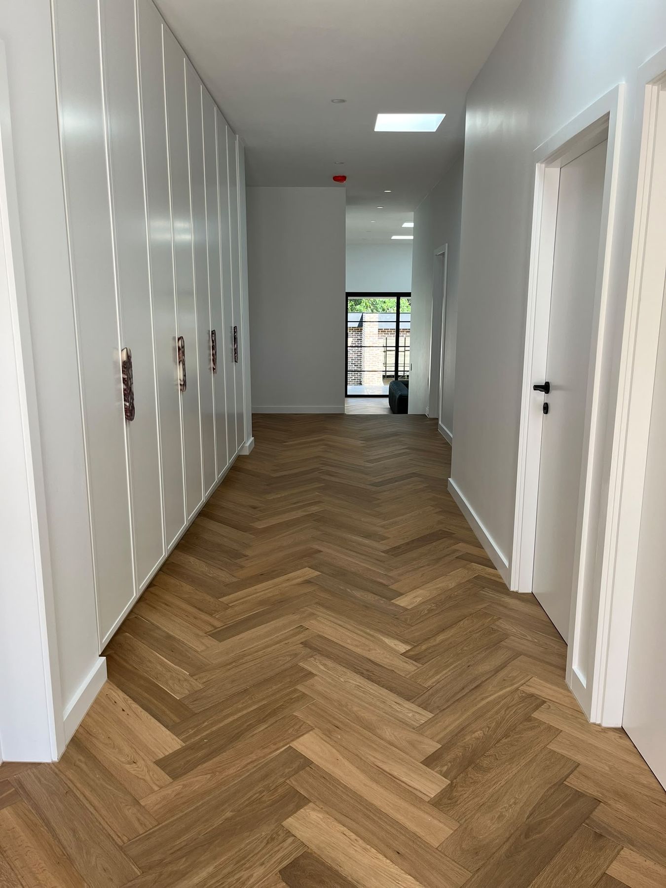 Hallway with herringbone oak flooring, full-height white joinery and a skylight