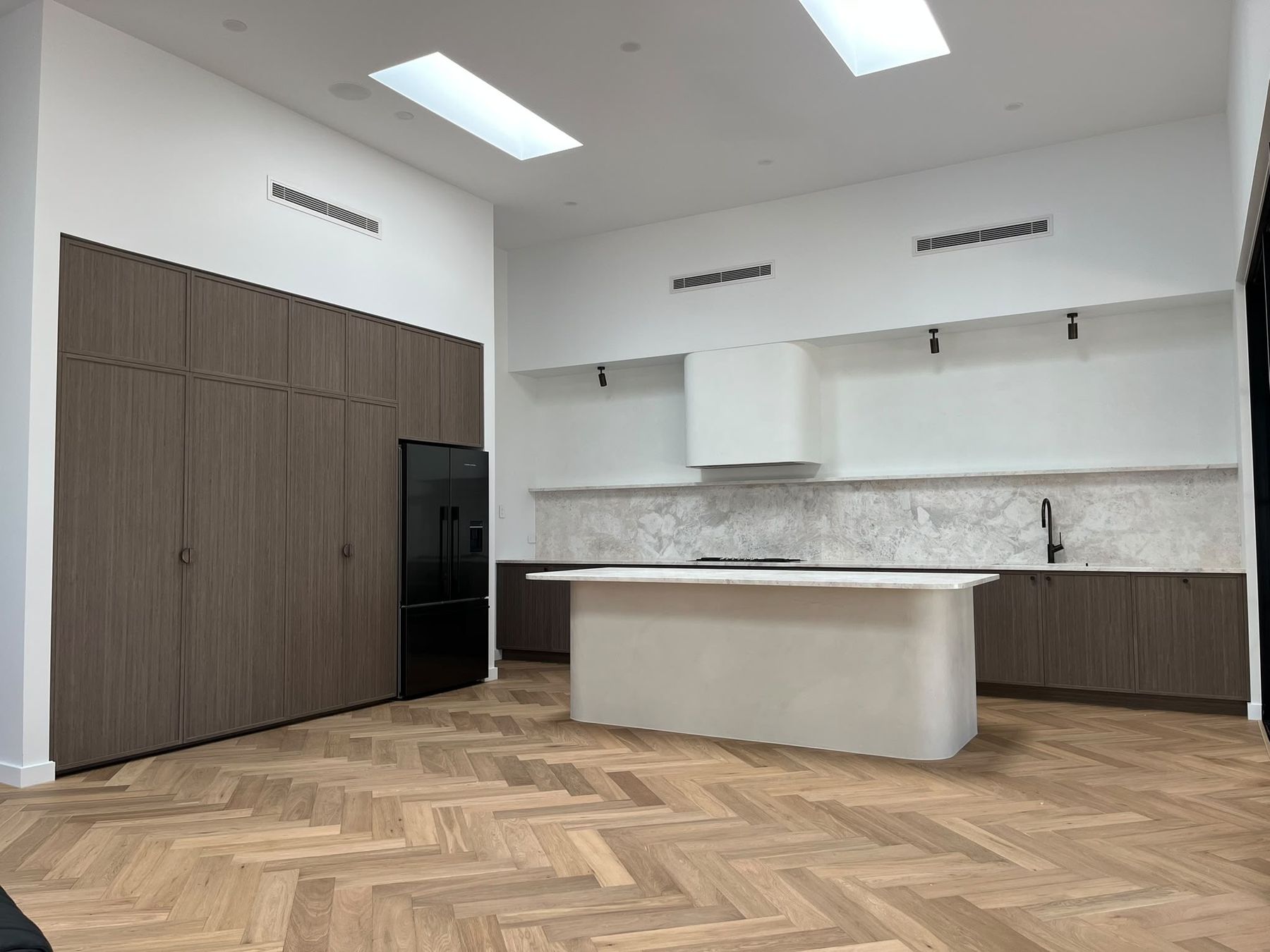 Renovated kitchen with herringbone oak flooring, curved plaster island and skylights