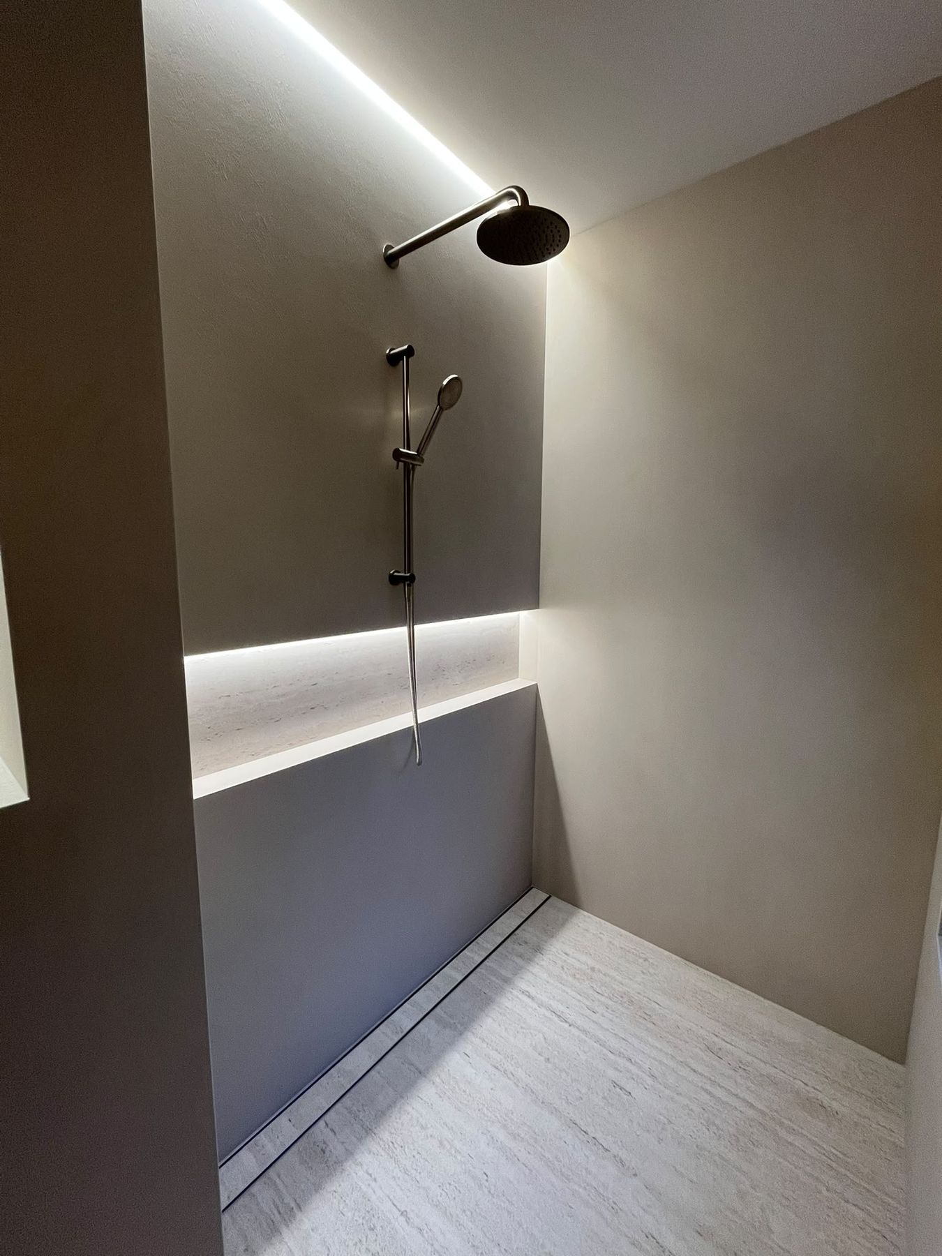 Microcement shower with a full-width travertine shelf niche and concealed LED lighting