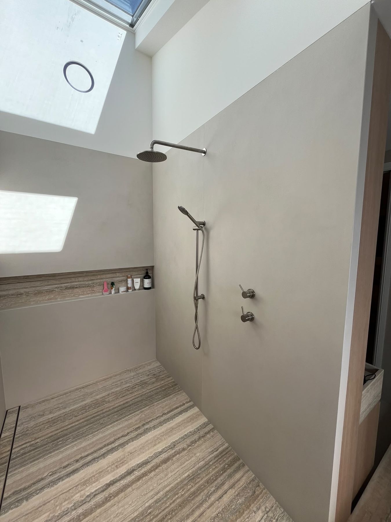 Walk-in shower with microcement walls, skylight above and travertine floor